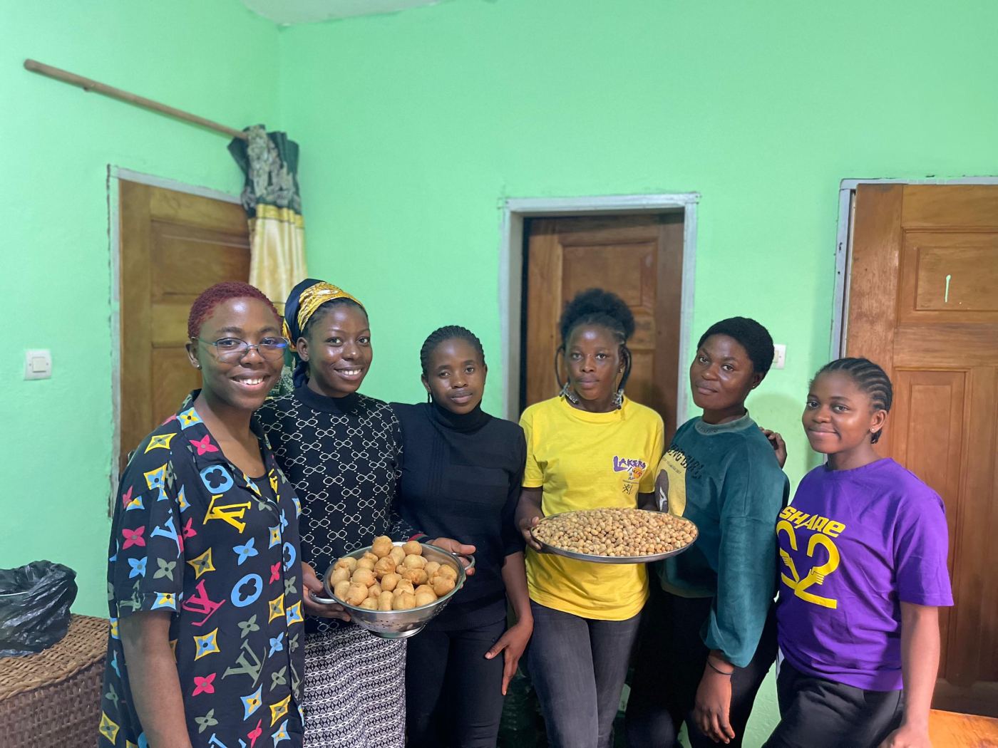 A trainer and smiling trainees holding up trays of doughnuts and roasted peanuts they made